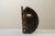 Brutalist mask sculpture made from a thick, concave, oval-shaped iron sheet. The piece features a rough but expressive...