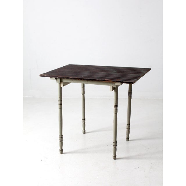 This is a vintage farmhouse side table. The rustic end table features a dark bead-board tabletop with slender, turned legs...