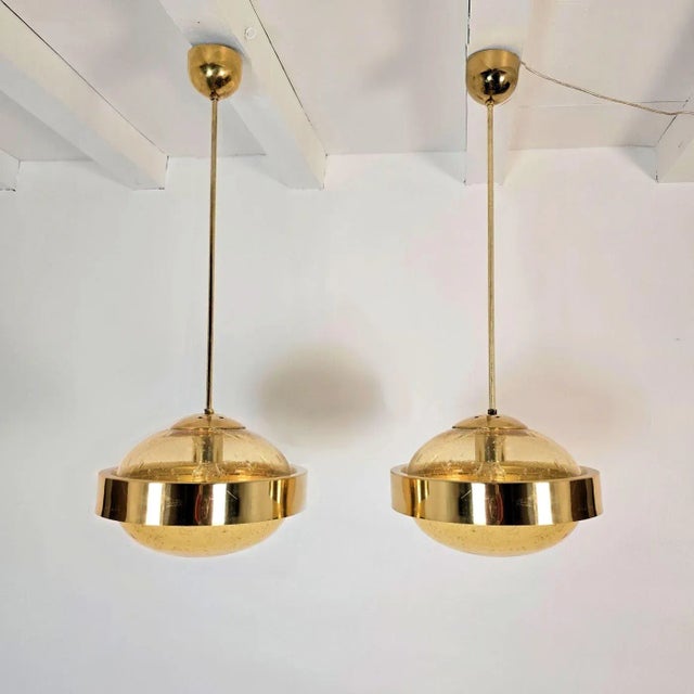 Pair of Mid-Century Modern pendant lights, Italy 1970s. The chandeliers are made of polished brass mounts and 2 hand-blown...