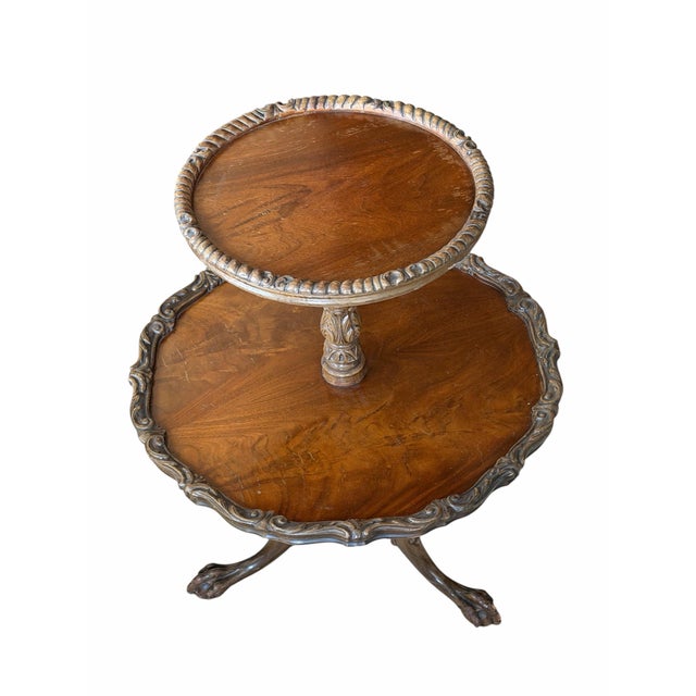 Antique two-tier side table with pie crust edges, carved tripod base, and claw feet. A classic decorative accent with warm...