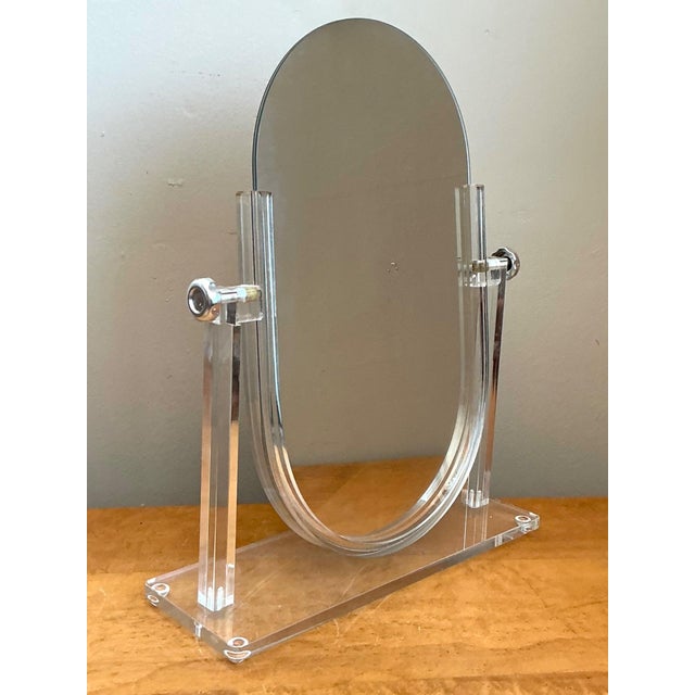 This mid-20th century vanity mirror is crafted from clear Lucite in an elegantly arched silhouette, a hallmark of the...