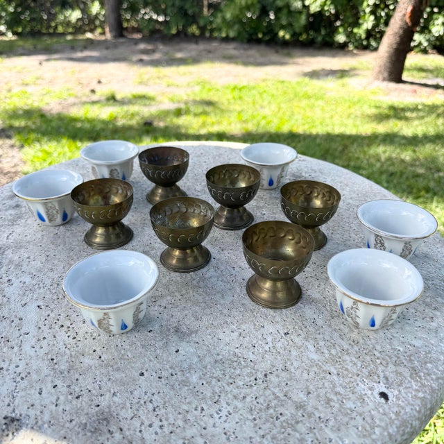 A charming set of vintage Israeli porcelain tea cups nestled within sculptural brass holders, blending delicate...