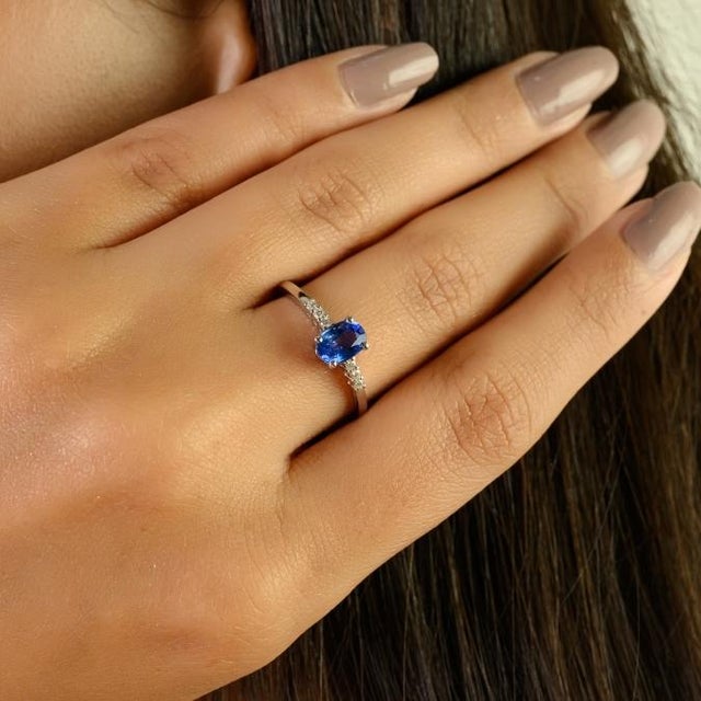 This elegant solitaire ring features a captivating oval-cut natural blue sapphire weighing approximately 0.76 carat,...