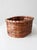 A vintage woven basket with an oval form and a warm honey-brown tone, finished with a deep red wrapped rim that adds...