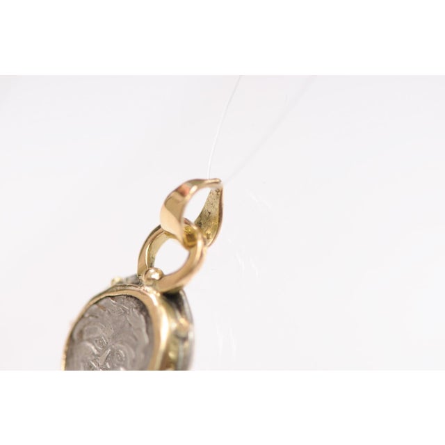 An AR Hemidrachm Greek coin pendant trimmed in sterling silver and 18 karat gold, circa 4th C, from Mysia, Parion. On the...