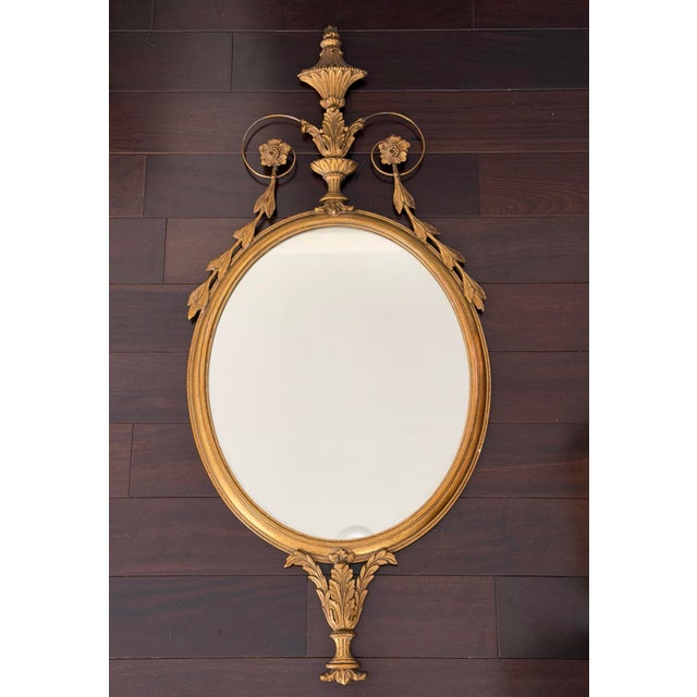 Elegant antique giltwood mirror in the Louis XVI taste, featuring a refined oval form crowned with a classical urn finial...