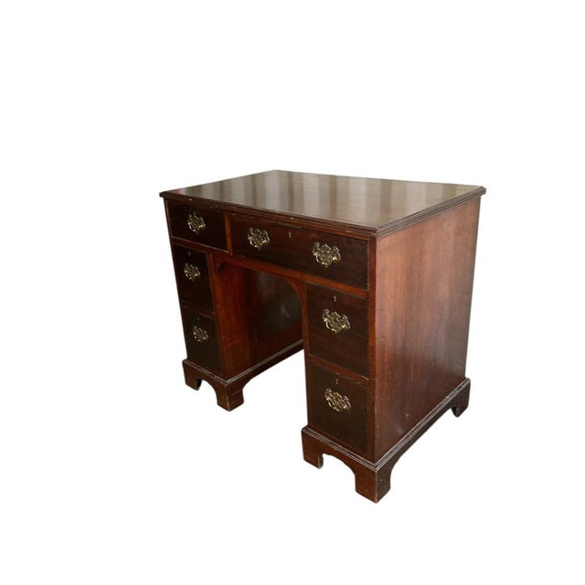 A George III crossbanded mahogany kneehole desk with a baized slide, over an arrangement of six drawers, with gilt handles...