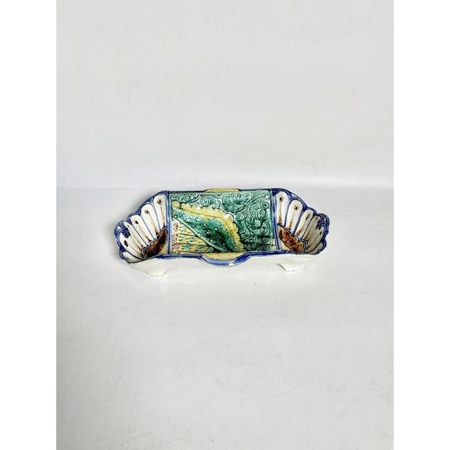A 1960s Italian ceramic serving dish with an elongated, undulating shape, resting on small feet. It is distinguished by...