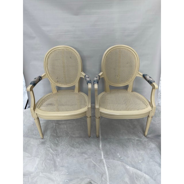 A matching pair of vintage carved wood French Louis XVI style arm chairs with woven cane seat and back. Each chair...