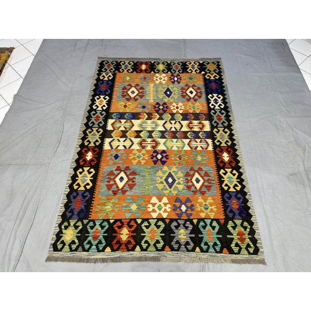 This Afghan Chobi flatweave kilim features a colorful tribal geometric design with horizontal bands and repeating diamond...