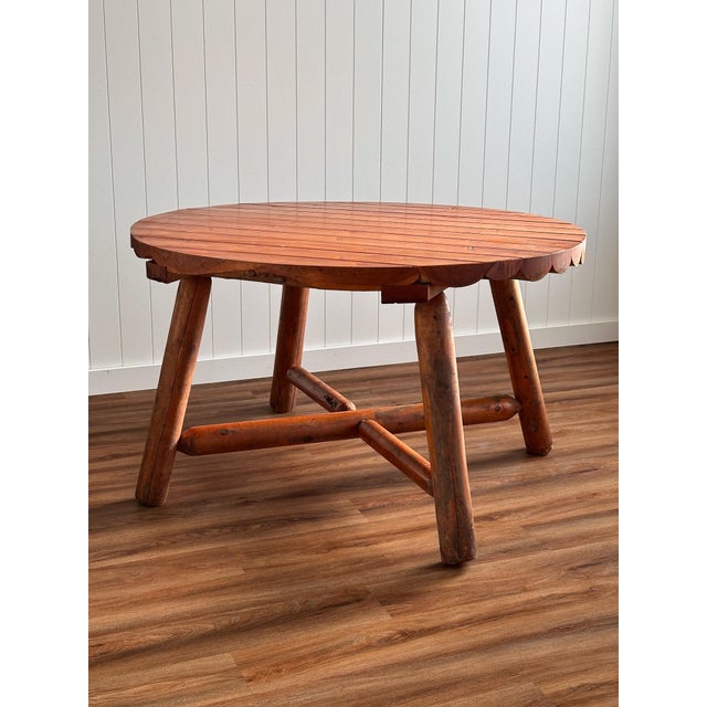 A vintage round dining table handcrafted from solid pine, featuring a scalloped slatted top and a sculptural log base with...
