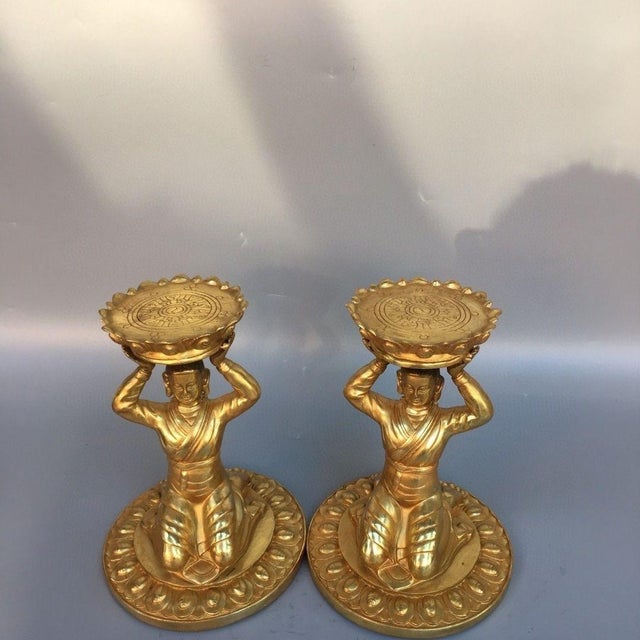 This is a striking vintage pair of gilt bronze candlesticks, each modelled as a kneeling figure holding a lotus-form...
