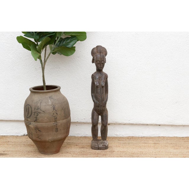 A graceful African Baule figure, standing at 40 inches tall with a base measuring approximately 7" x 6". Originating from...
