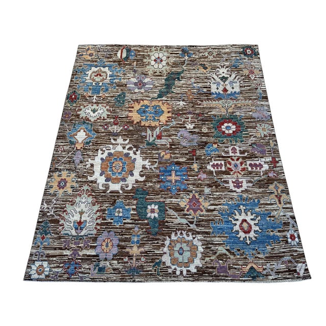 Handmade from high-quality wool, this Oushak rug features oversized floral motifs across a chocolate brown field streaked...
