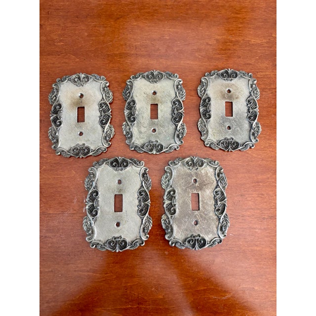 This substantial set of vintage metal light switch plates features richly textured surfaces framed by intricate Regency-...