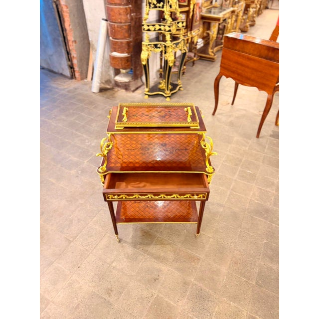 A striking French Louis XVI-style two-tier serving table featuring rich mahogany tones and beautifully detailed gilt...