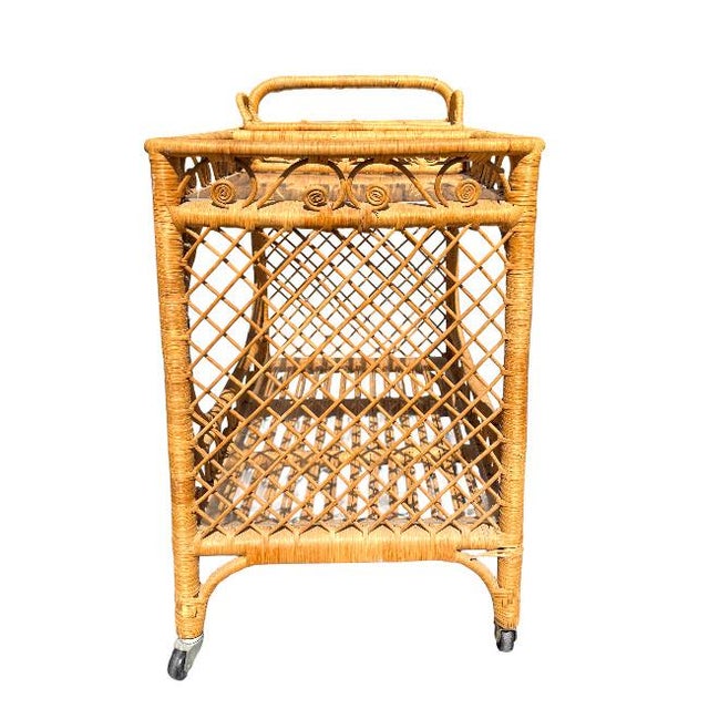 Charming vintage rattan bar cart featuring a beautifully woven frame with decorative fiddle leaf–style scroll detailing...