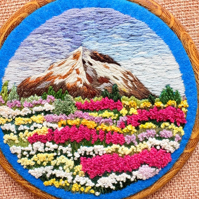 Bring the breathtaking beauty of a sun-drenched alpine meadow into your home. This exquisite hand-embroidered wall art...