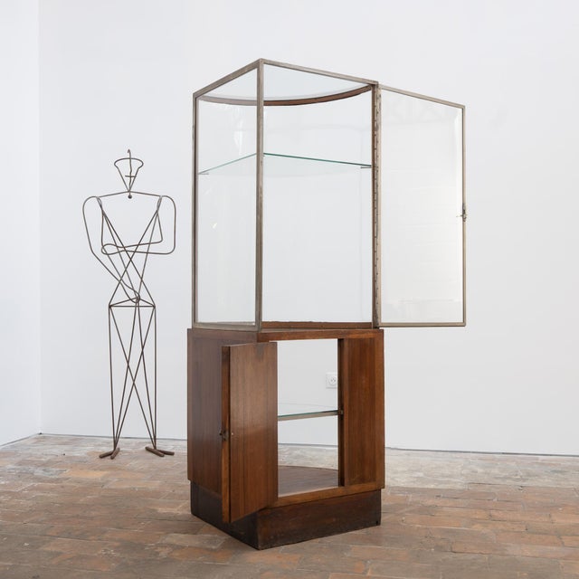 Art Deco corner display cabinet in wood and glass, with a rounded nickel-plated brass frame on the front. The upper glass...