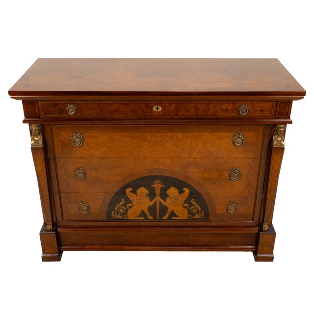 Decorative Empire-style chest of drawers featuring a bold Neoclassical design with opposing griffins flanking a torch...