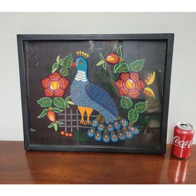 Colorful mid century embroidered peacock surrounded by flowers on a black ground. Protected in a shadowbox frame and ready...