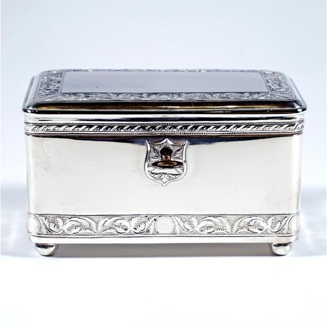Silver lidded box of rectangular shape, with straight sides and rounded corners and edges, standing on four flattened...