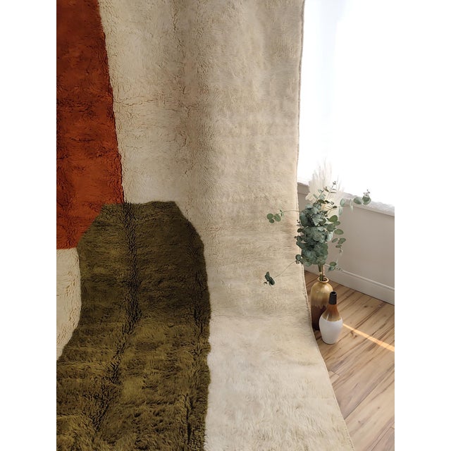 A bold contemporary color-block Moroccan rug — clean fields of rust-orange and olive-green float across a plush cream...