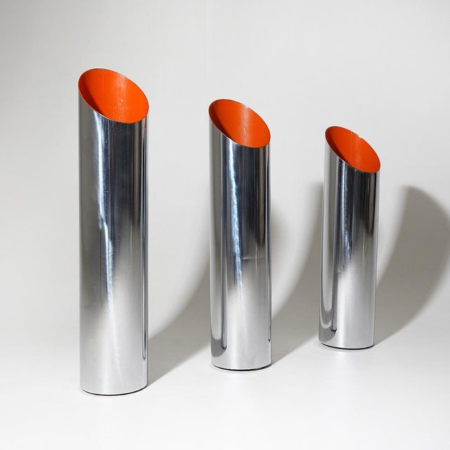 Three chromed metal umbrella stands from the 1970s, characterised by an essential cylindrical shape ending with a...