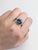 A London blue topaz rests in a deep, steely blue at the centre of this solid 14K white gold ring, encircled by sixteen...