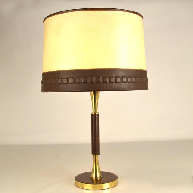 High-quality 1960's table lamp is hand crafted from brass and dark brown leather with an elegant tapered stem and the base...