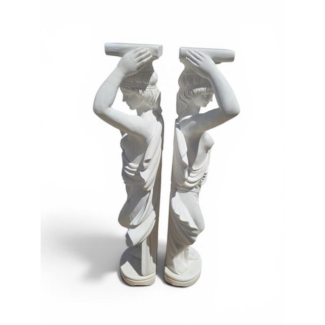 Exceptional pair of classical pedestals carved in white marble, each adorned with two sculpted figures. Crafted in Italy,...
