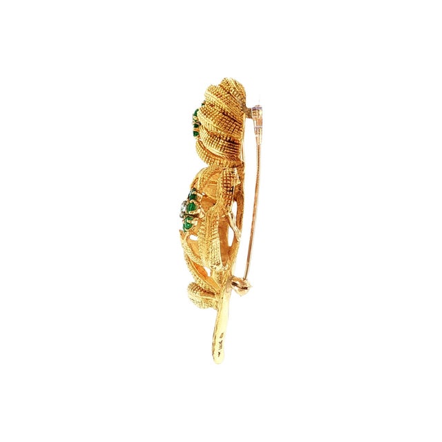 A mid-century 18k gold and platinum textured floral brooch. Features round green emeralds, total weight 0.75 carats....