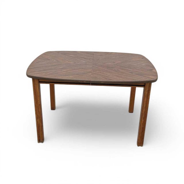 A compact mid-century modern dining table with a walnut-look laminate top arranged in a radiating bookmatch-style pattern...