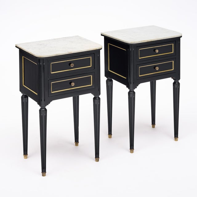 A refined pair of French Louis XVI style side tables featuring ebonized wood, gilt-brass accents and beautifully veined...