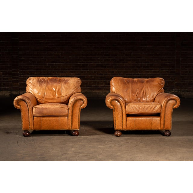 Handsome pair of full-grain brown leather club chairs built with the familiar weight and presence of classic English...