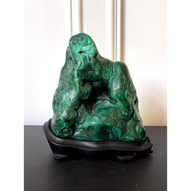 A natural malachite rock specimen in form of a mountain peak with striking green and black colors fitted on a wood stand...