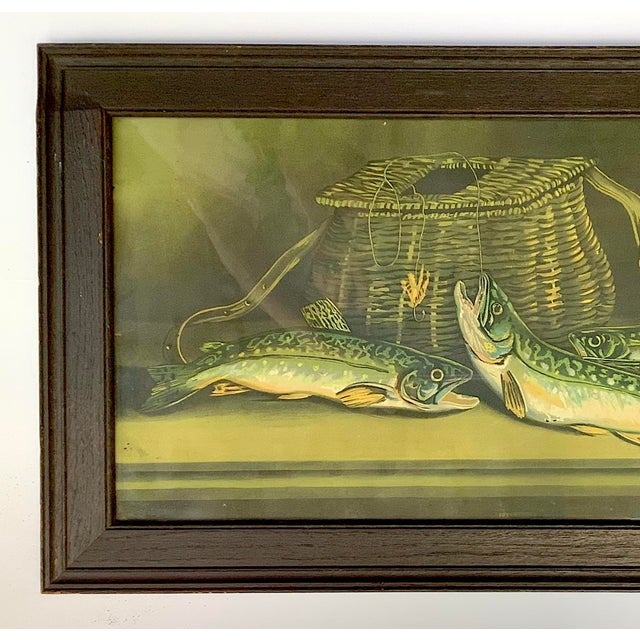Beautiful colors on this circa 1930s lithograph of catch of the day with trout, creel, fishing fly in original fumed oak...