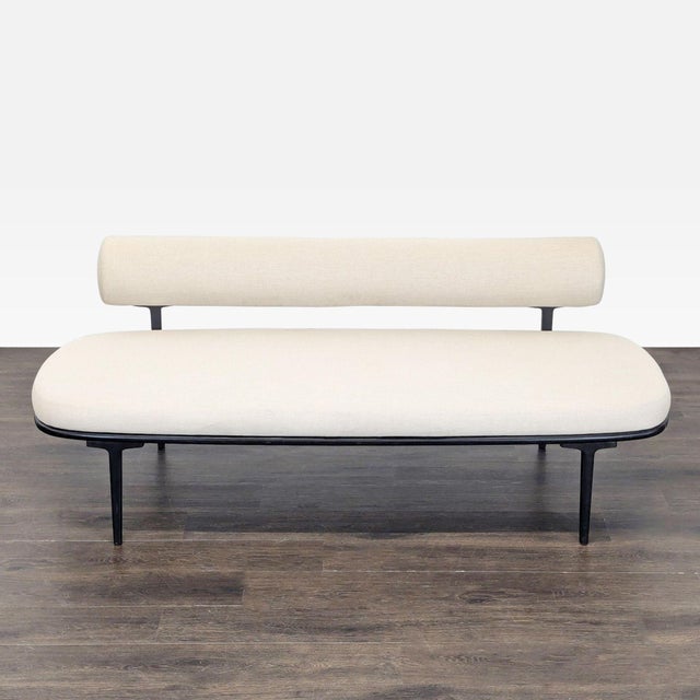 This CB2 sofa features a sleek and simple design with cream upholstery and black metal legs. The slim backrest and...