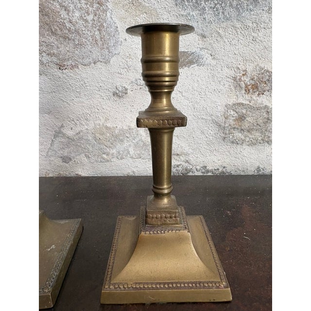 Pair of Victorian brass candlesticks, circa 1860s. Baluster-turned stem on a square, stepped, beaded base, with a campana-...