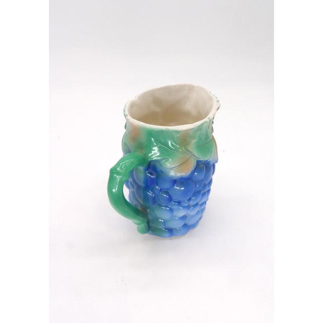 This pitcher features grapes with a green vine handle and leaves around the rim. It is 4.5" tall. The bottom is marked...