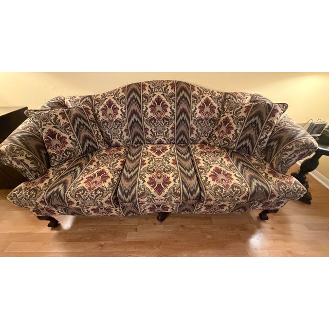 Traditional serpentine camelback sofa featuring carved claw-and-ball feet, sweeping rolled arms, and richly patterned...