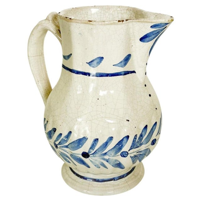 A charming 19th-century earthenware pitcher, hand-decorated with stylized floral motifs in cobalt blue tones on a creamy...
