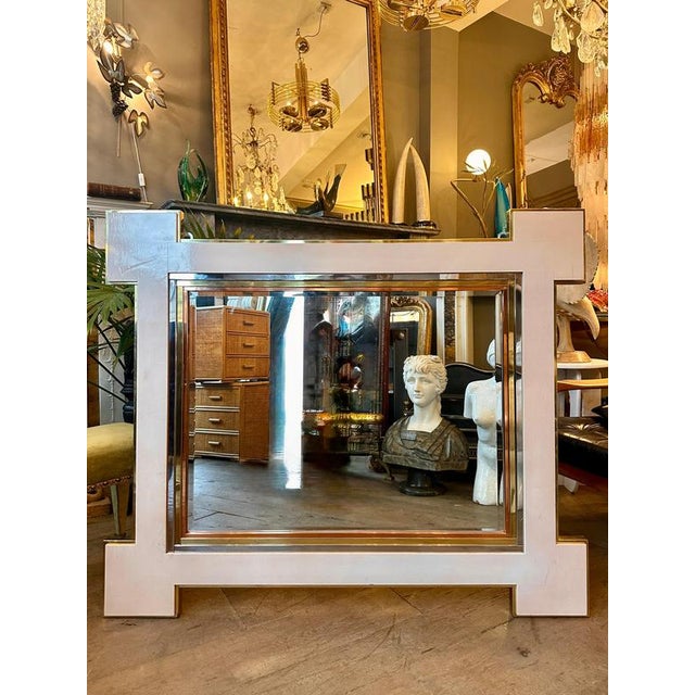 A French late 20th century circa 1970 Cream Lacquered and Brass wall mirror. The 'Dog Ear" or 'Kit Kat" shape design of...