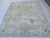 An ivory field with soft blue floral vines defines this handmade Oushak wool rug. Taupe and sand-colored leaves weave...