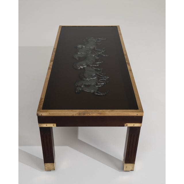 A sculptural mid-century coffee table featuring a glass top with a decorative relief panel beneath, set within a wood and...