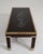 A sculptural mid-century coffee table featuring a glass top with a decorative relief panel beneath, set within a wood and...
