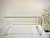 A clean and architectural tubular steel coffee table featuring a white enamel-finished frame and floating glass top. The...
