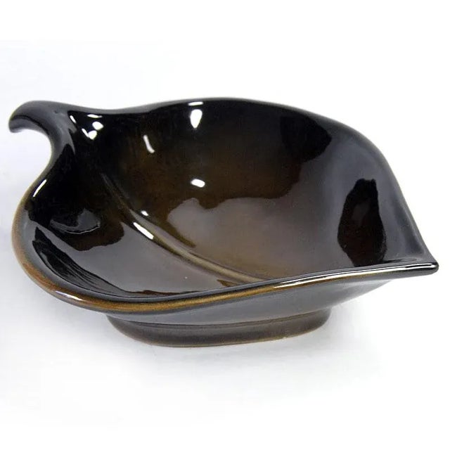 A striking ceramic platter in the shape of a delicate leaf. It is decorated with a highly lustrous glaze in dark brown and...