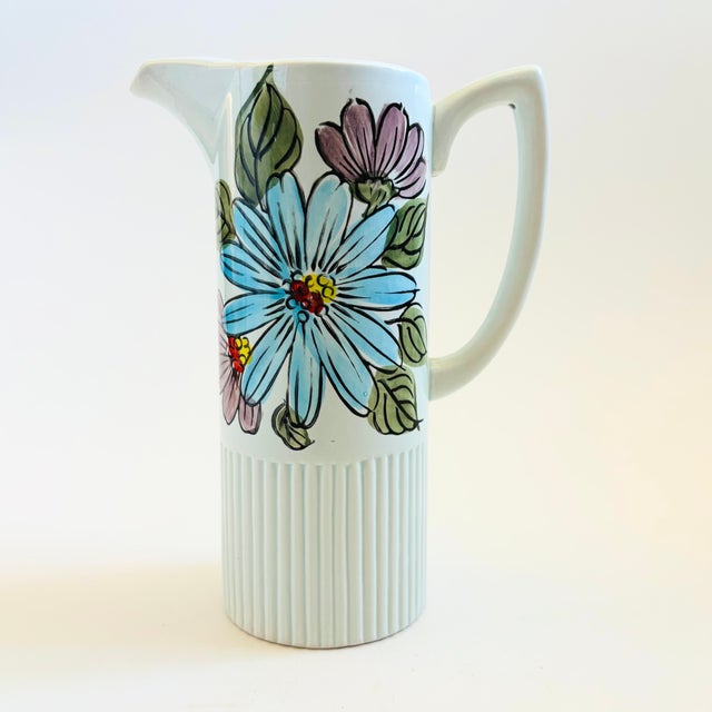 A mid century porcelain pitcher. White glaze featuring a colorful floral design on the upper portion and a ribbed base....