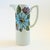 A mid century porcelain pitcher. White glaze featuring a colorful floral design on the upper portion and a ribbed base....